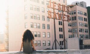 Djevojka sjedi na rubu zgrade/balkona i gleda natpis Isus spašava