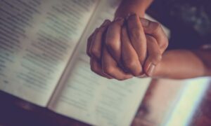 Ruke sklopljene u molitvu, iznad Biblije