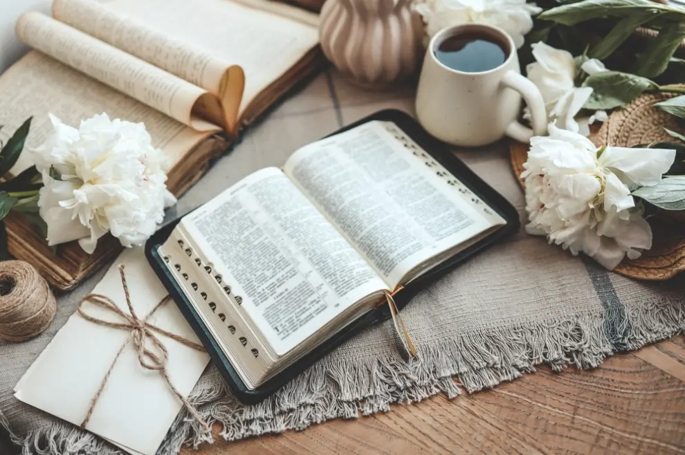 otvorena Biblija na stolu s kavom i cvijećem