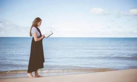 Bosa djevojka na plaži uz ocean, čita knjigu