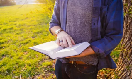 Muškarac na livadi čita Bibliju, moli se